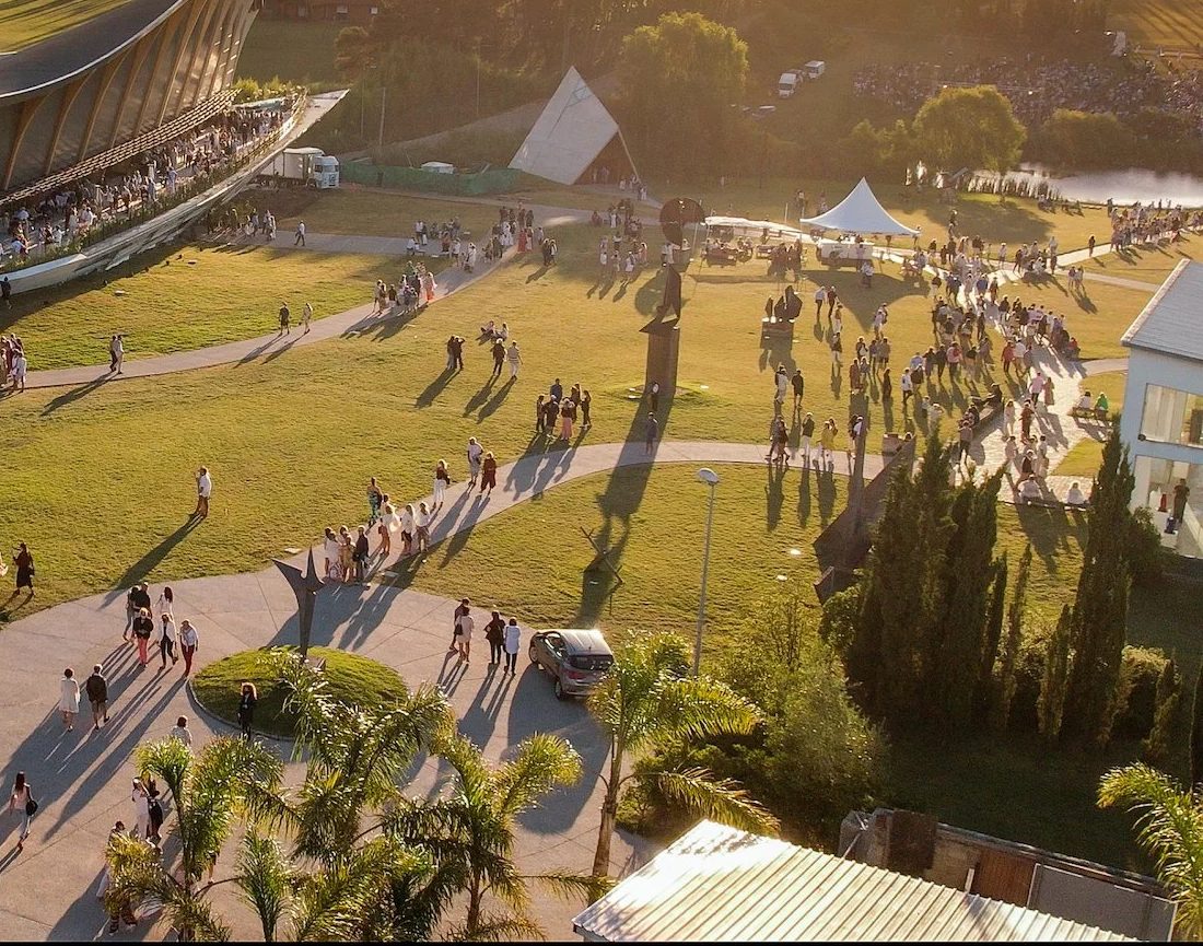Personas recorriendo el parque de esculturas del MACA al atardecer, con una carpa blanca